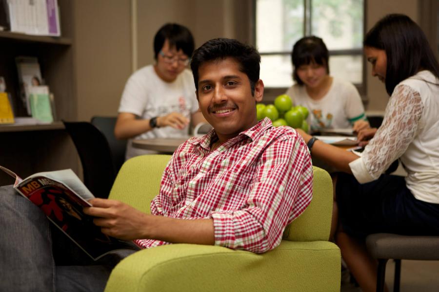 A student sits in a green armchair and reads while inside the Student Services office.