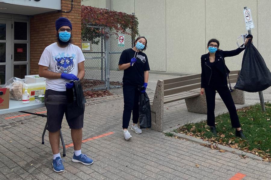 Three students pose outside, one holds up a filled garbage bag.