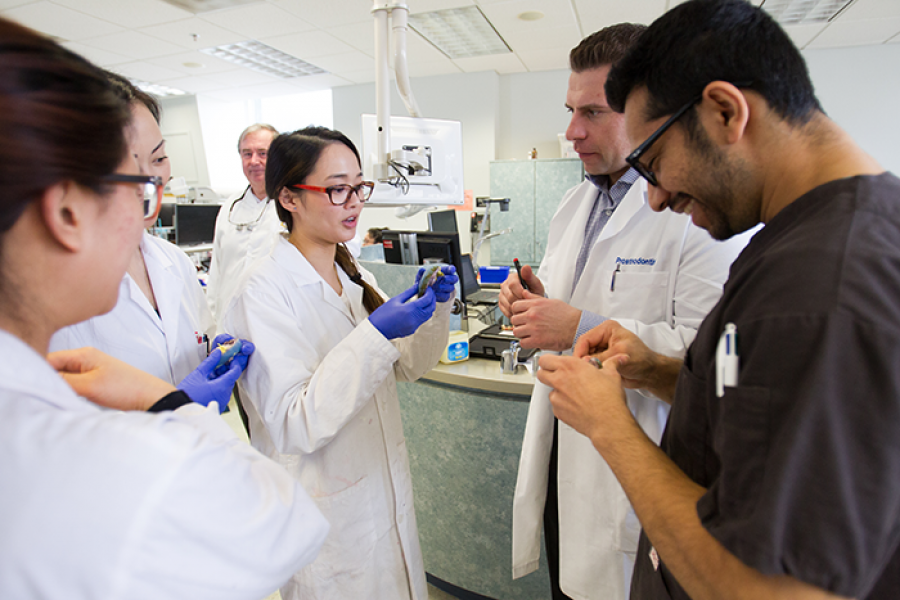 A group of students in lab coats and one in scrubs reviewing a dental cast.