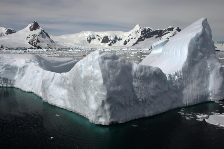 Large iceberg peaking out from waters with glacier in the background