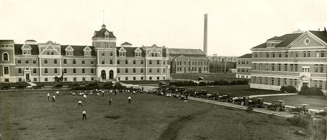 A black and white photo from 1930 showing the E1 engineering building and the old dorms. In the Quad, several people and playing sports.