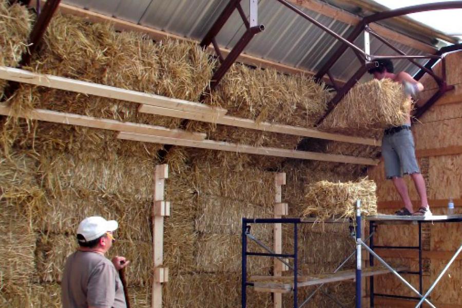 A man works on building an alternative village building by placing straw bales into a structure.