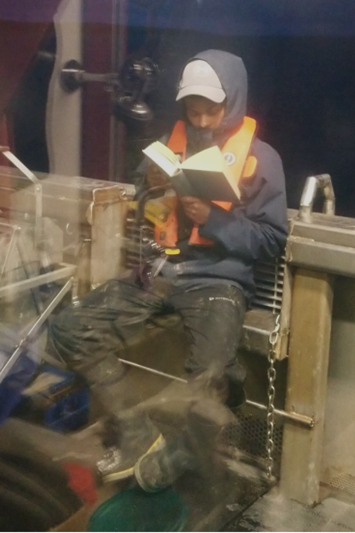 Durell Desmond sits reading a book bundled up on a research vessel