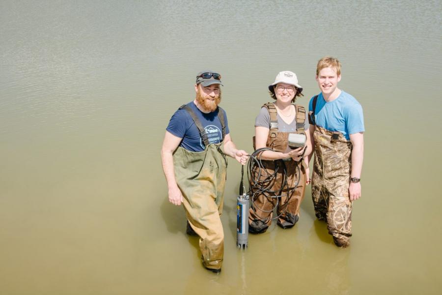 Mark Hanson and two students standing in water looking upwards at camera.
