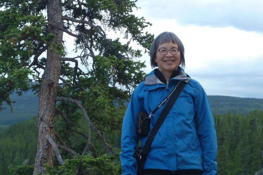 Nancy chow standing outdoors wearing a blue jacket beside a tree.