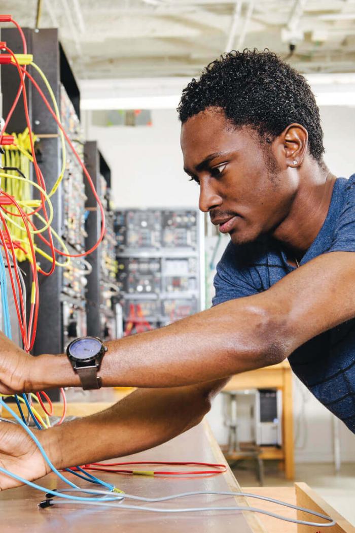 An engineering student carefully tests wires on an electric board.