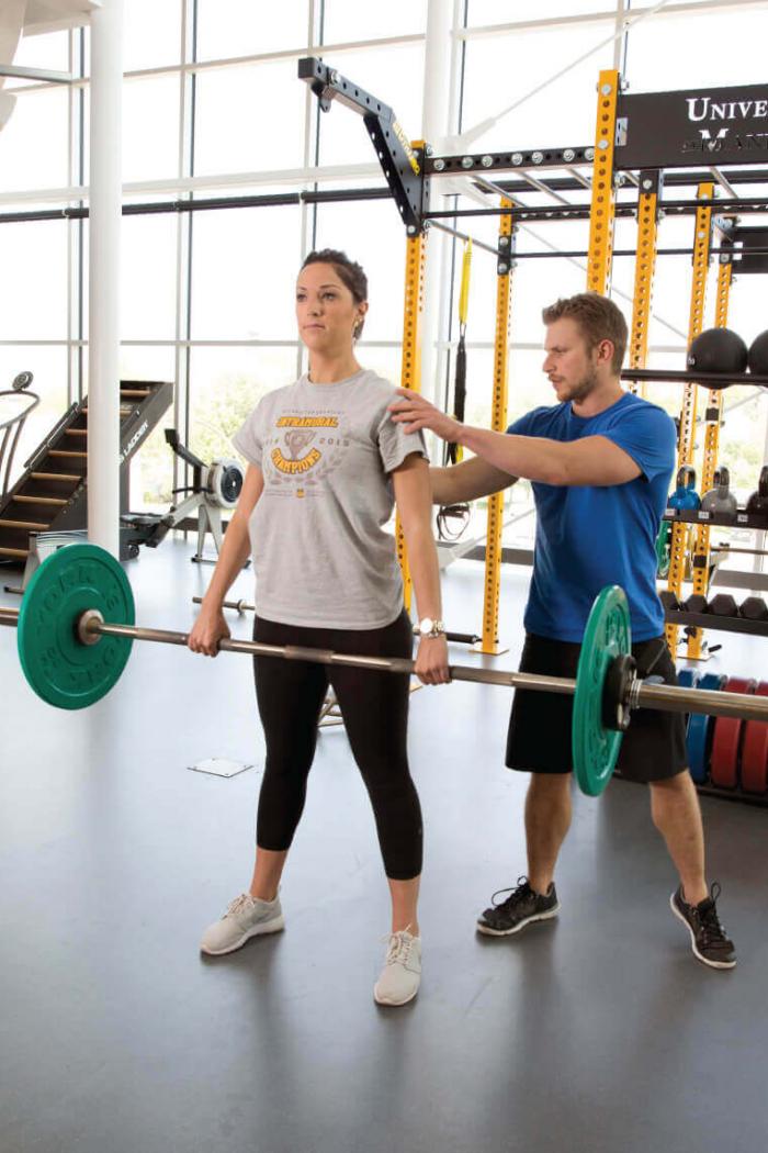 A certified fitness instructor correcting the form of a student.