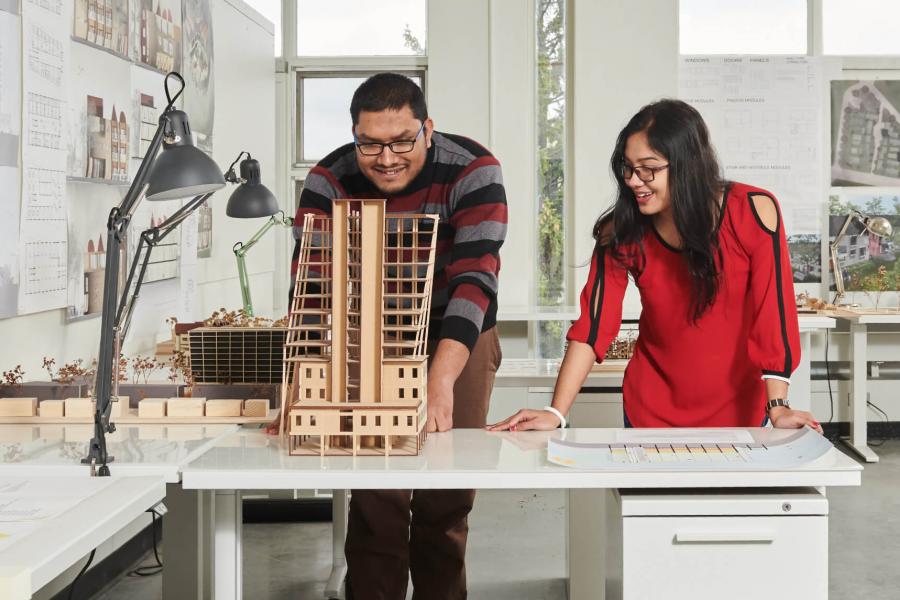 Two Faculty of Architecture students stand at a desk and look at a project they are working on together.