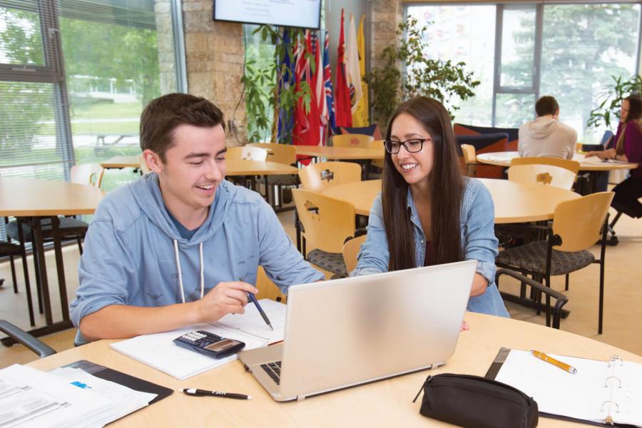 Two indigenous students sit together at a round table studying at Migizii Agamik-Bald Eagle Lodge.