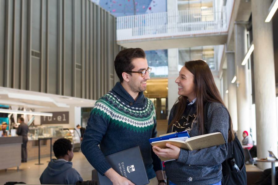 Two students stand together talking inside the Active Living Centre.