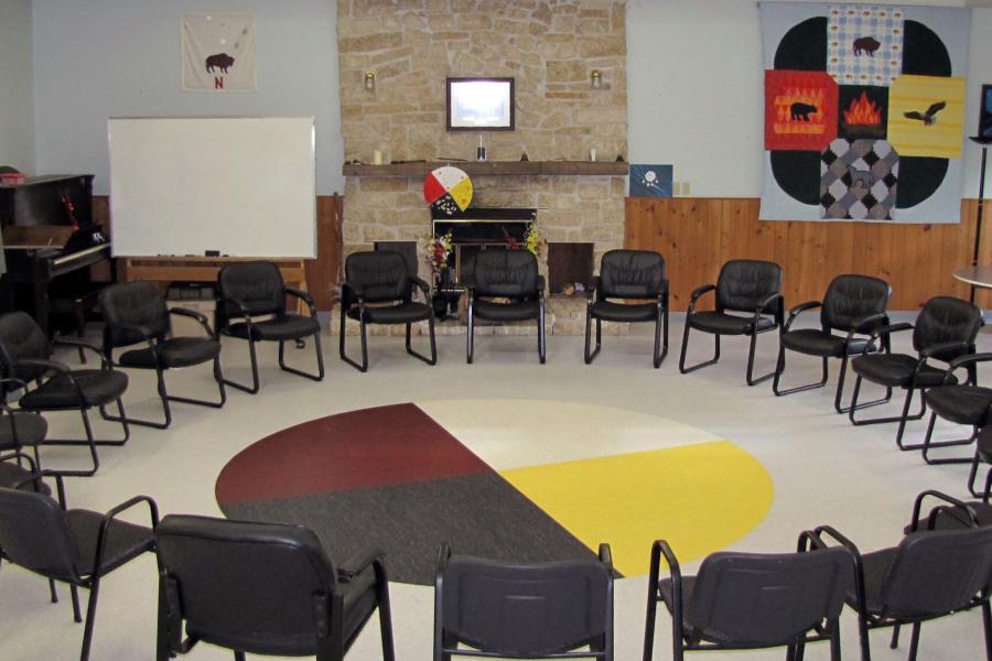 A room with chairs forming a circle around a medicine wheel on the floor. 