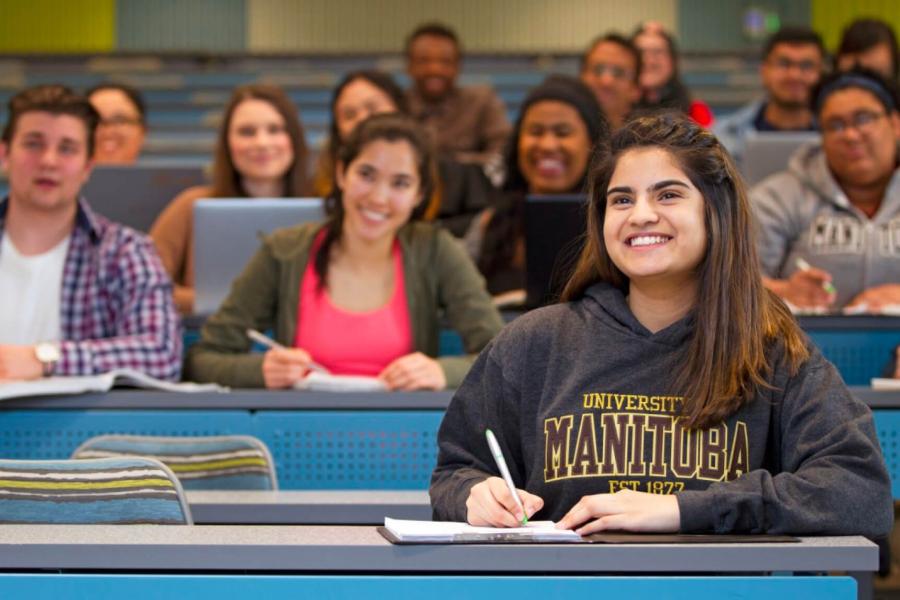 A classroom of smiling attentive student taking notes. 