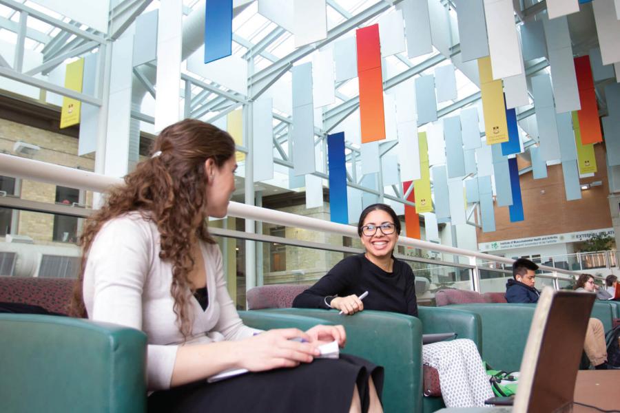 Two students sitting together in the University of Manitoba Bannatyne campus Buhler atrium.