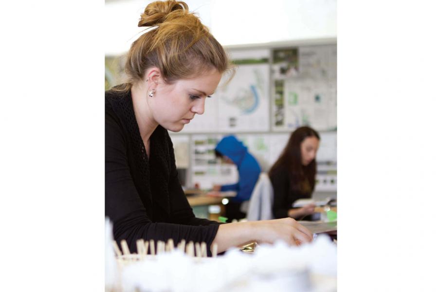 An architecture student carefully works on a project at her desk.