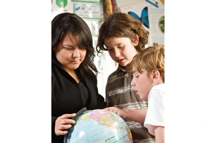 Three inquisitive children huddle around a globe looking for a location.