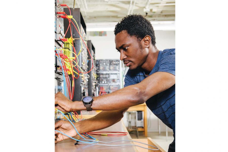 An engineering student carefully tests wires on an electric board.