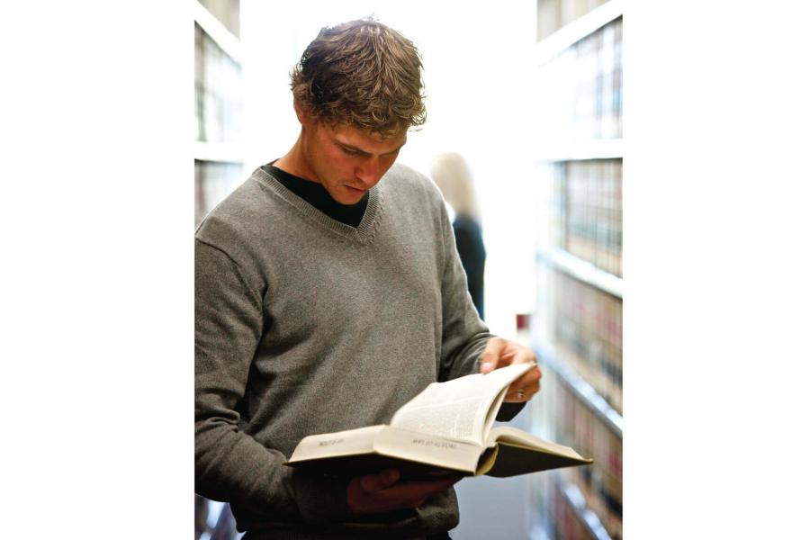 A law student skimming a book in an isle within the library stacks.