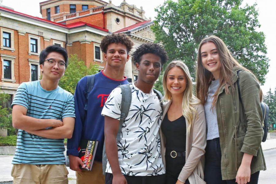 A group of five undergraduate students stand together in front of the University of Manitoba Administration building.