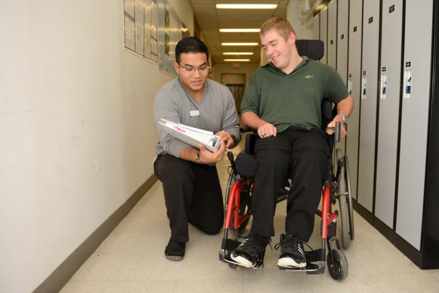 An occupational therapist kneels down to show a patient something written in a book.