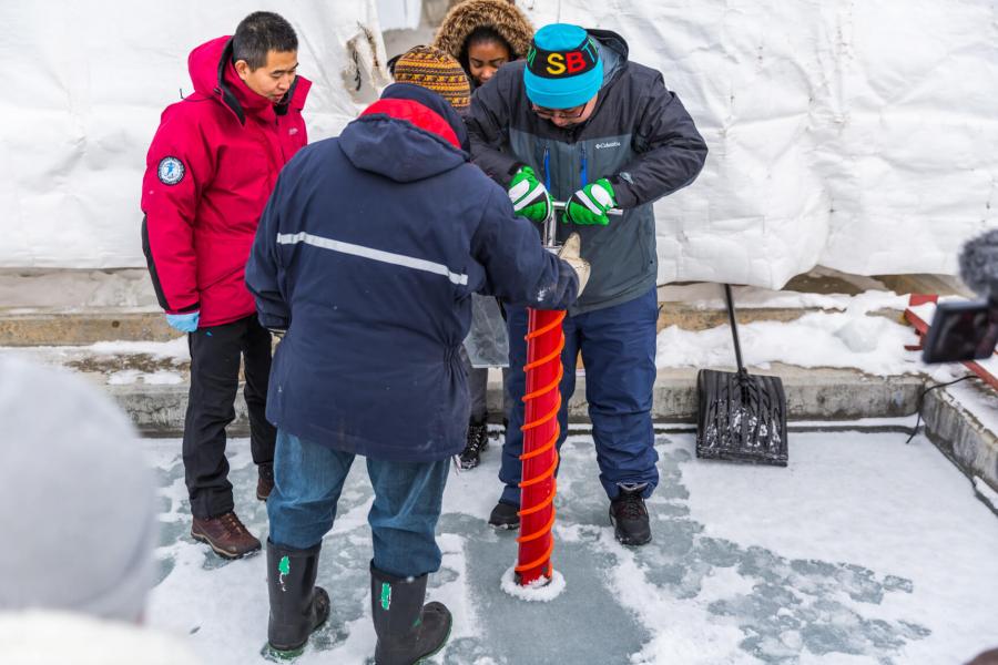 Researchers and students drill a hole into ice.