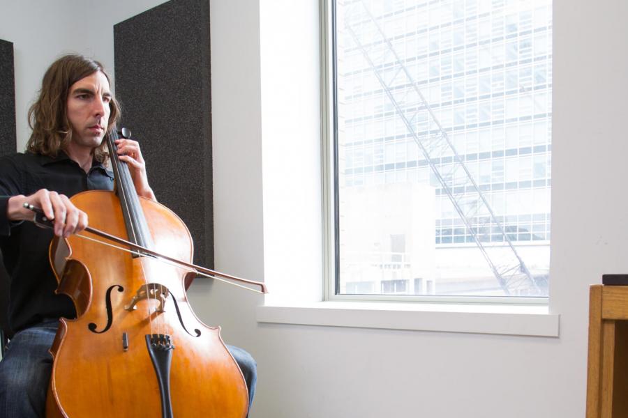 A student plays an instrument near a large window in a practice room.