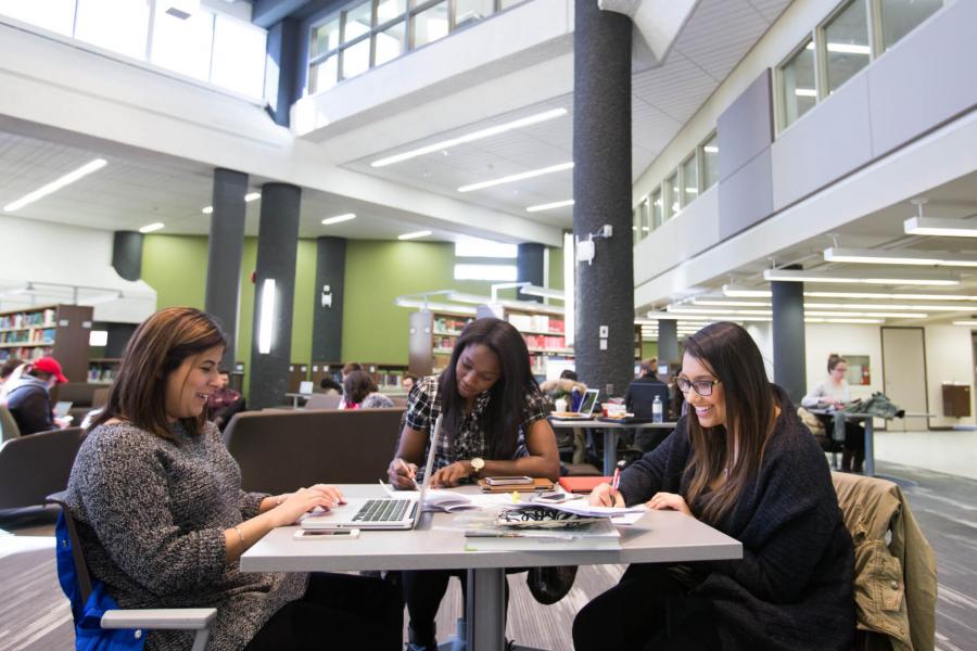 Three students seated around a table studying in a library.