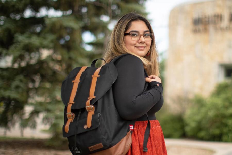 A University of Manitoba student stands holding a backpack outdoors. 