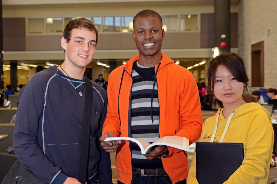 Three international students stand together in a library.