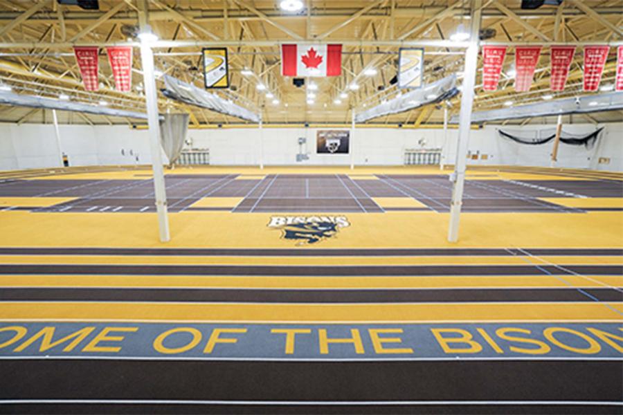 Large indoor sports complex. The slogan "home of the bisons" is printed on the floor. In the centre are three badminton courts with a running track around the outside.