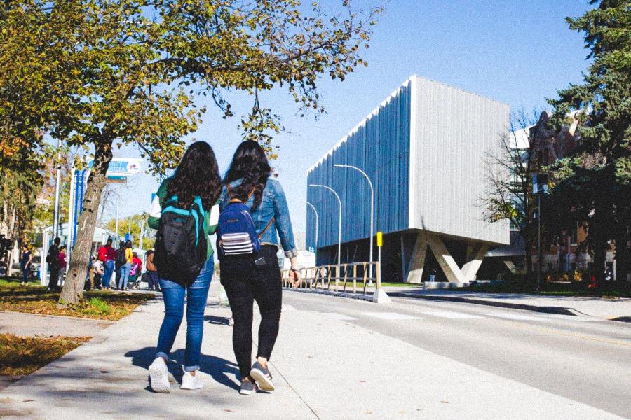 An image of two students outside on UM's Fort Garry Campus, walking towards Art Lab building.