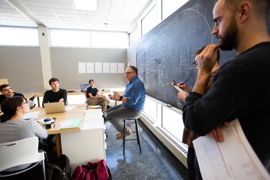 An instructor seated on a stool in front of a chalkboard talks to a class in the John A. Russell Building.