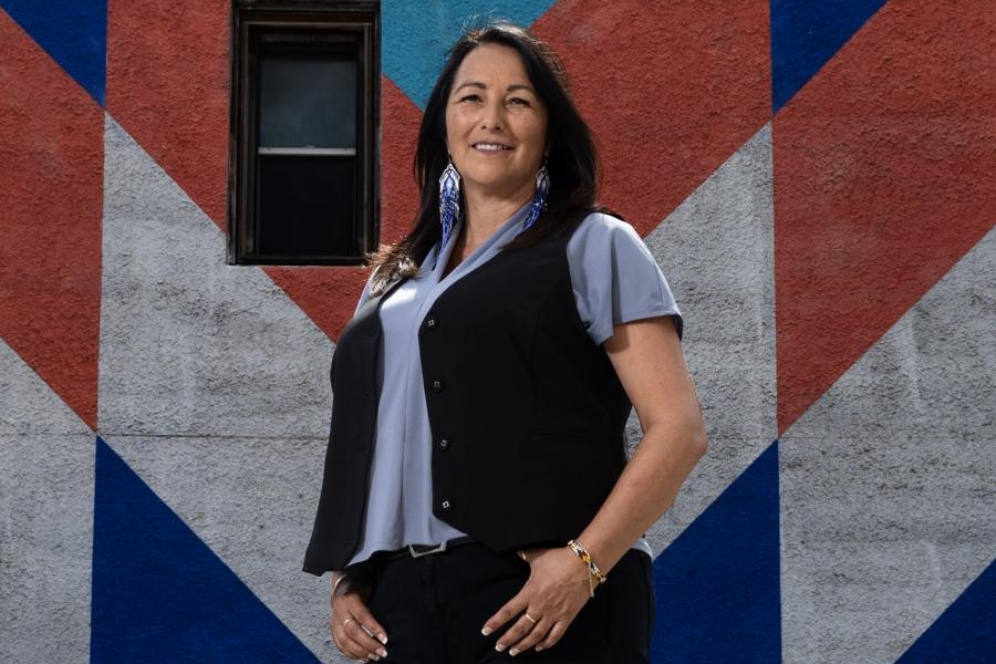 A woman in a black jacket and t-shirt standing in front of a colorful wall.