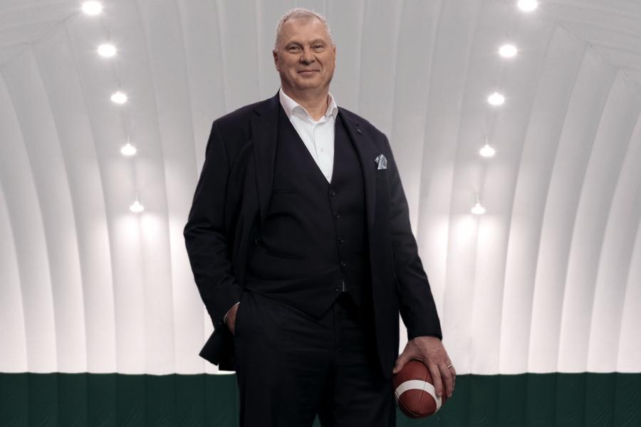 A smiling older gentlemen in a business suit holding a football.