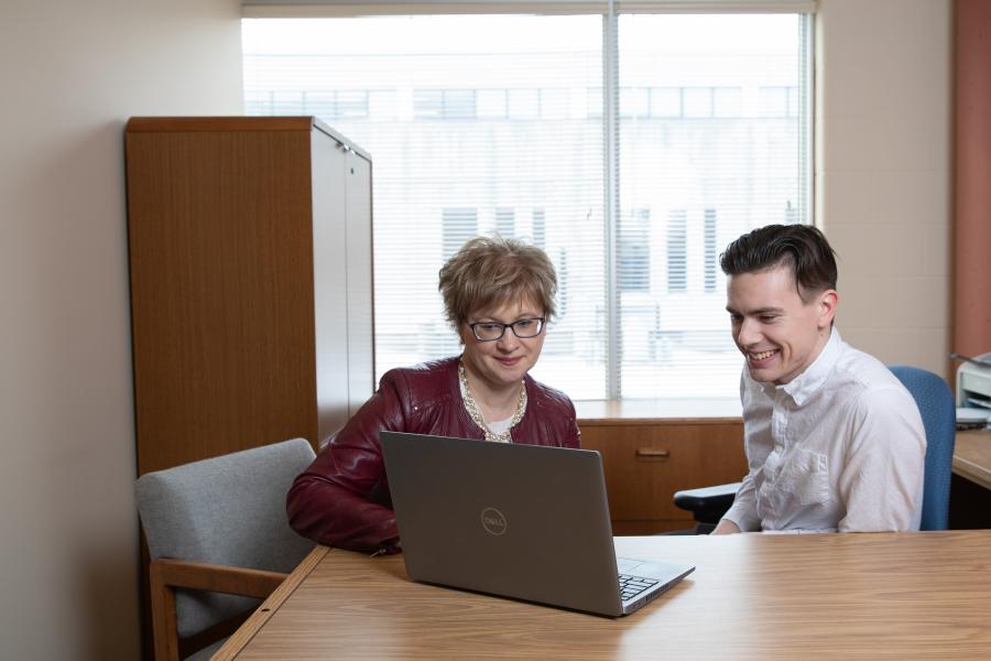 Two people seated at a desk looking at a laptop screen in a office.
