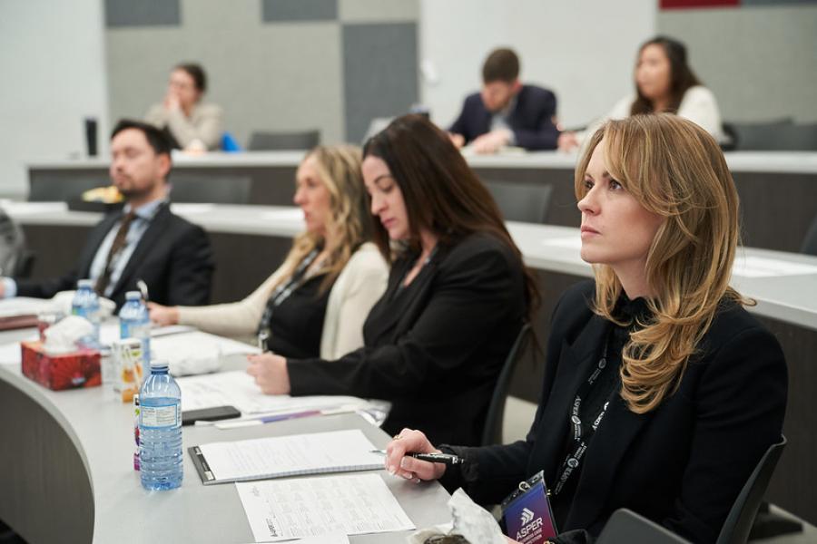 A group of people sitting in a classroom looking up and taking notes.