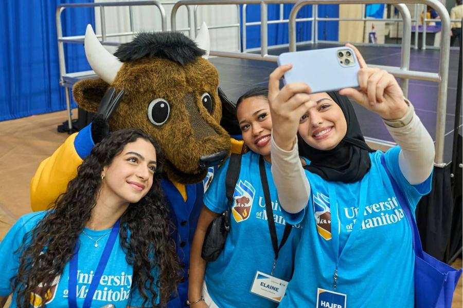 Three student volunteers take a selfie together with Billy the Bison.