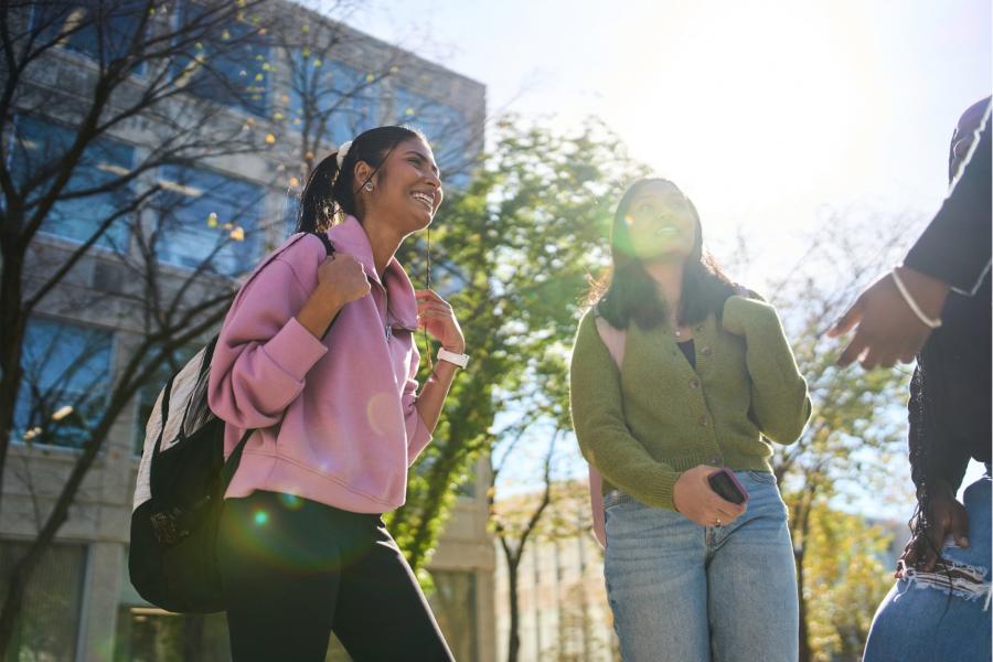 Two students smile as they stand outside by a tree and building.