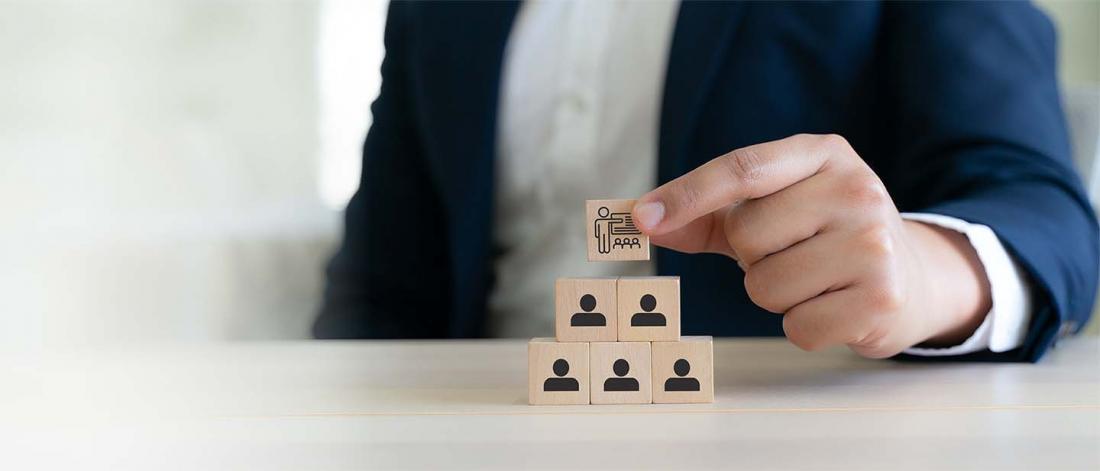 The photograph shows a businessperson arranging wooden organizational-chart blocks on a desk.
