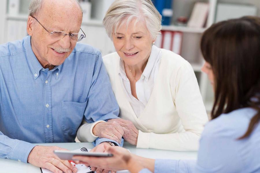 The smiling elderly couple receiving advice from a female counselor who is showing them a tablet