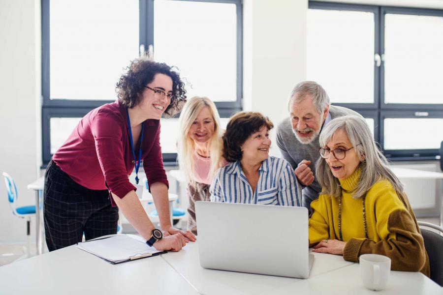 A woman is teaching a group of elderly to use a laptop