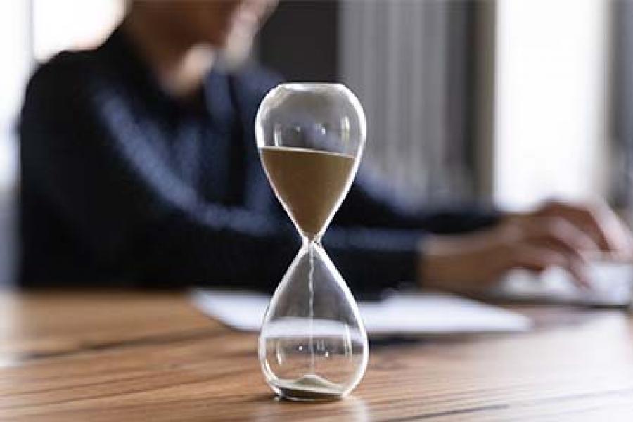Close-up view of the hourglass with a woman working on a laptop.