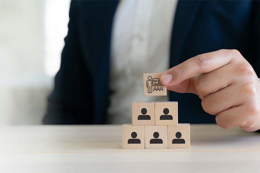 The photograph shows a businessperson arranging wooden organizational-chart blocks on a desk.