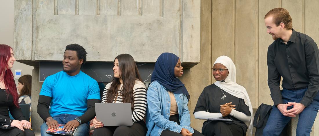 a group of students sitting along a bench talking with each other