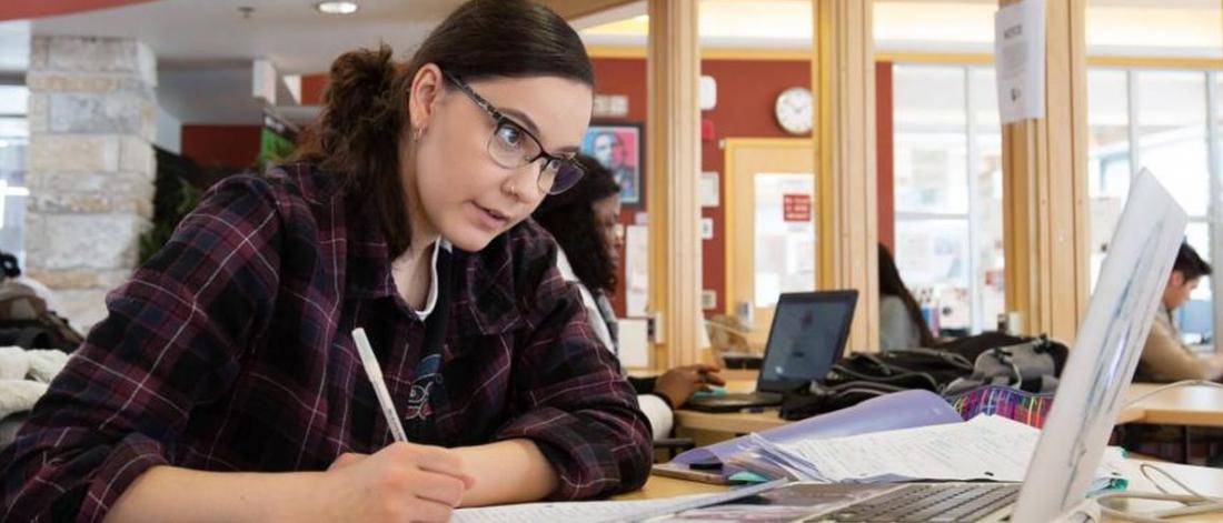 Student looking at laptop while writing in a notebook.