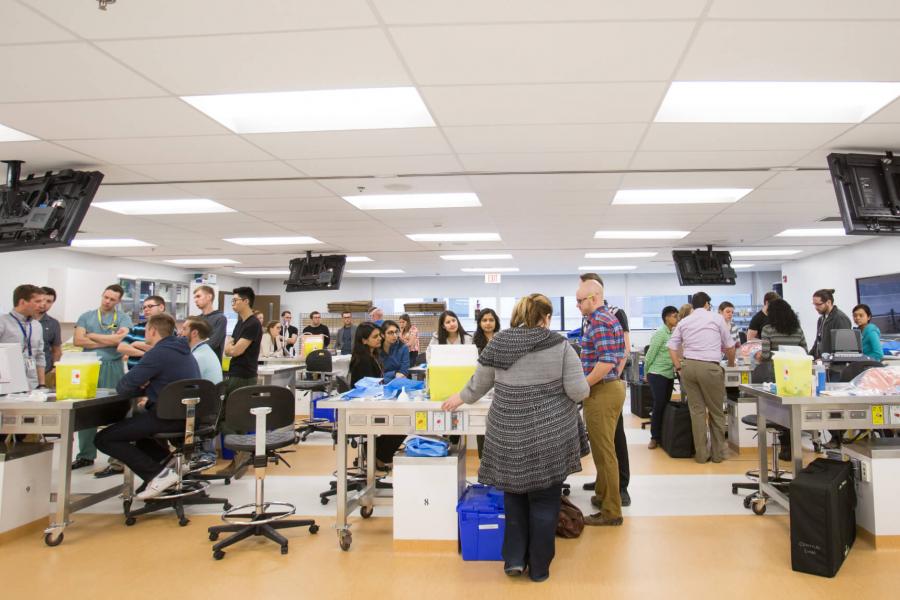 Medicine students work in a large room in groups at separate tables.
