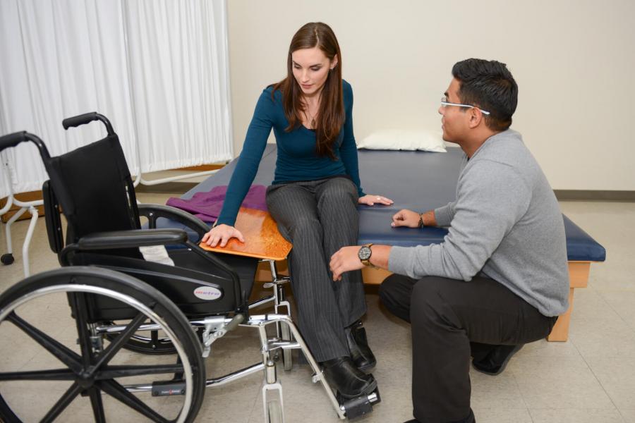 A Rehabilitation Sciences student assists a client into a wheelchair from a bed.