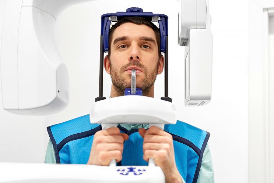 Patient in a blue protective vest has his teeth scanned in a large imaging machine.