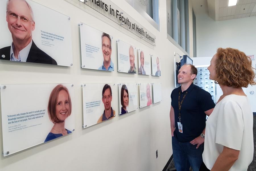 Two people standing , looking at a wall of photo plaques.