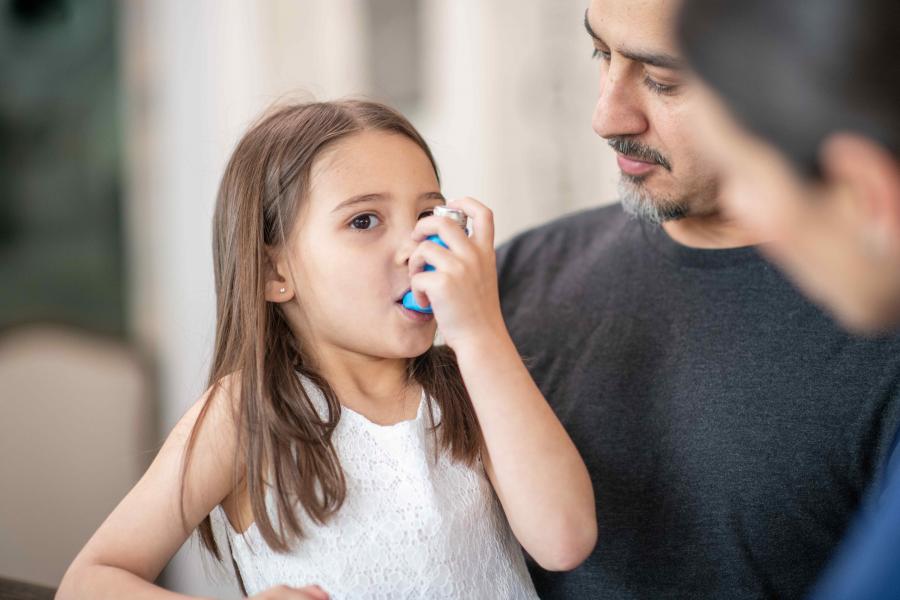 A child sits on their parents lap and practises using an inhaler.