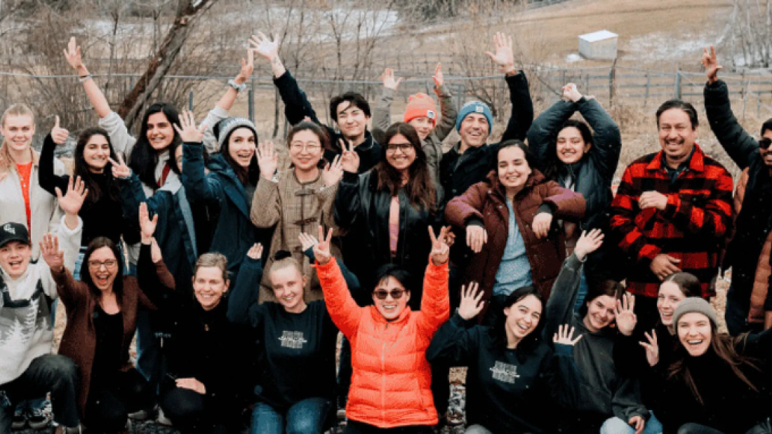 Group of students and community members outdoors, smiling and waving together during a gathering or retreat.